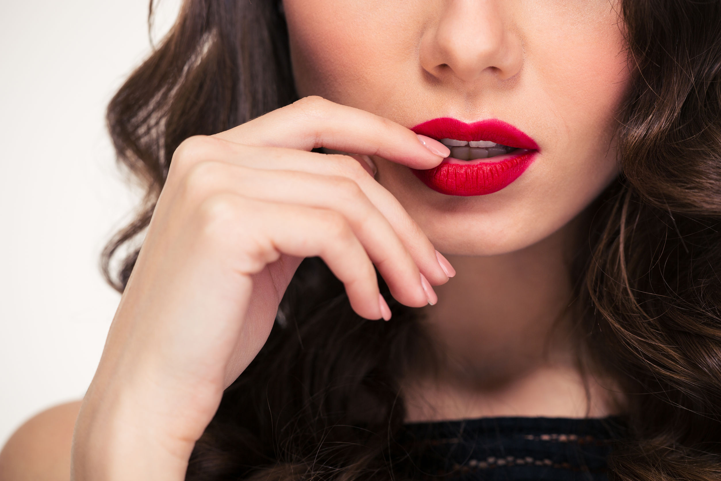 Closeup of tempting bright red lips of young curly woman touched by her hand