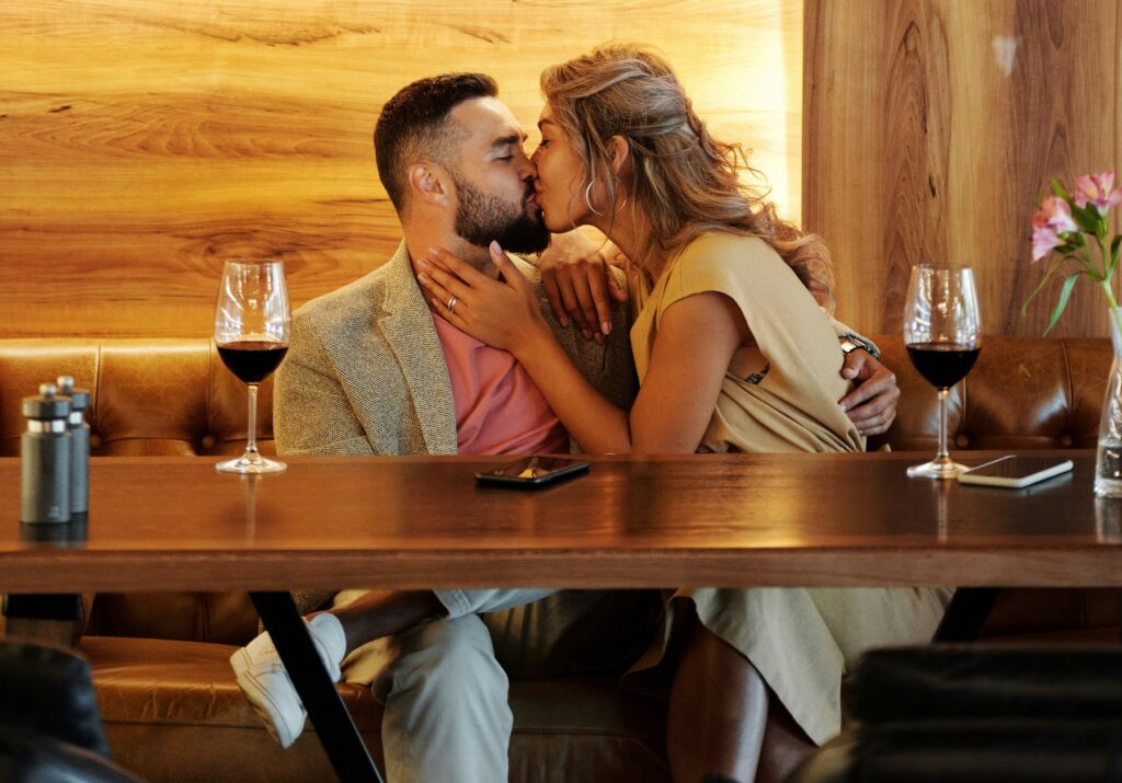 Swinger Couple Kissing on a Couch Near the Table With Wine Glasses