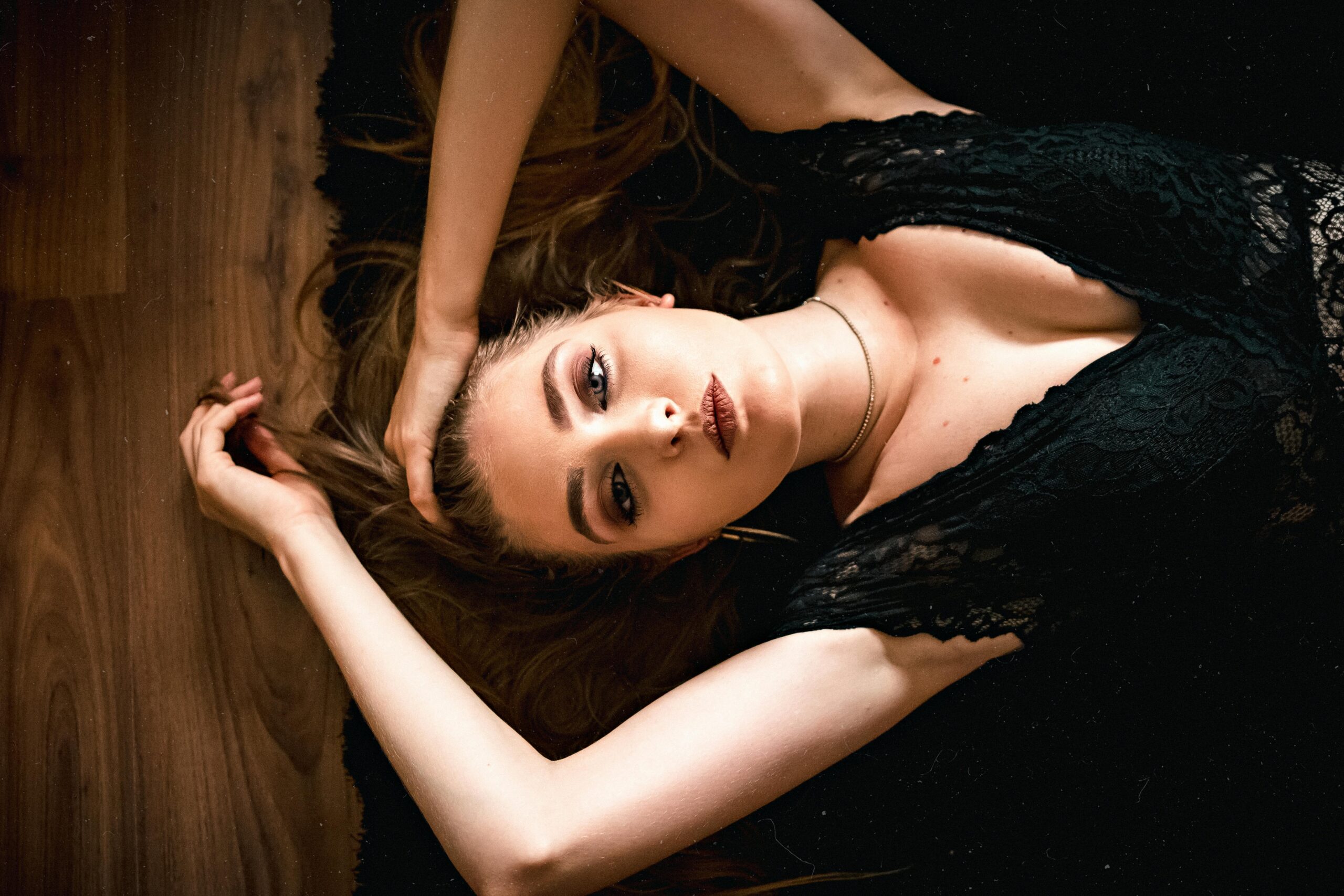 Alluring young woman touching hair while lying on floor