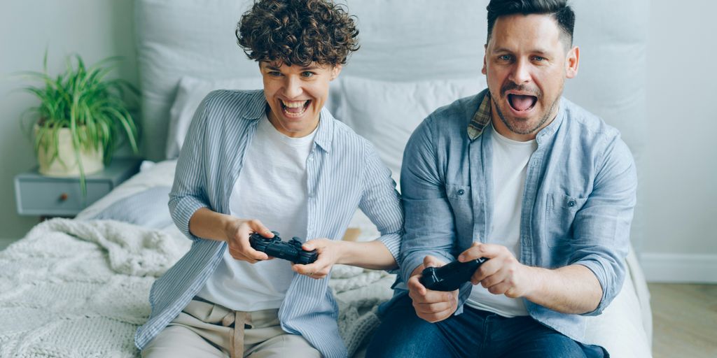 a man and a woman sitting on a bed playing a video game