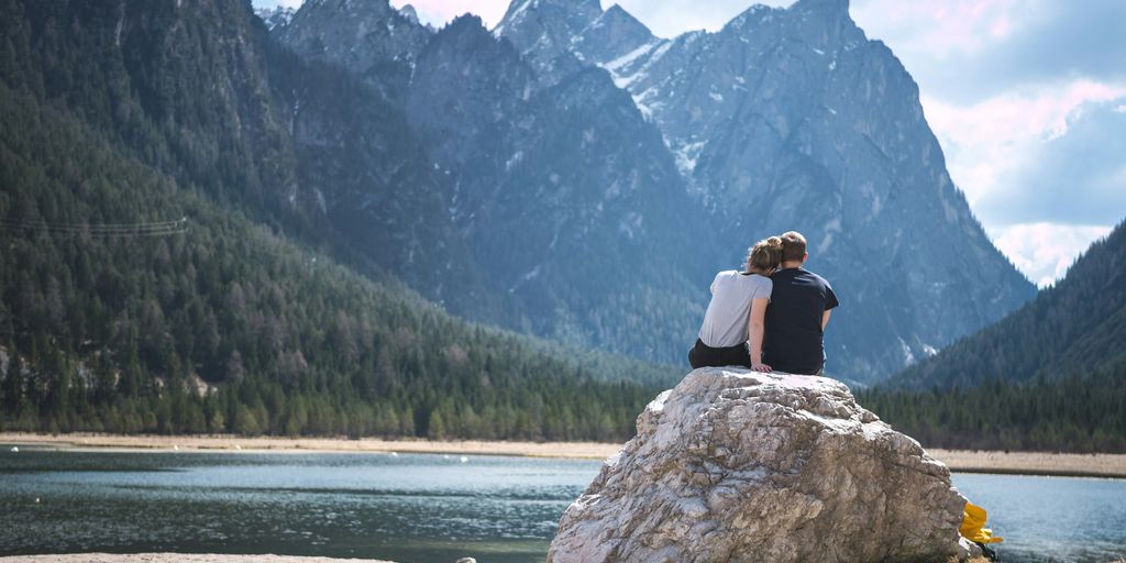 couples sitting in the rock while in front of a lake and mountains  