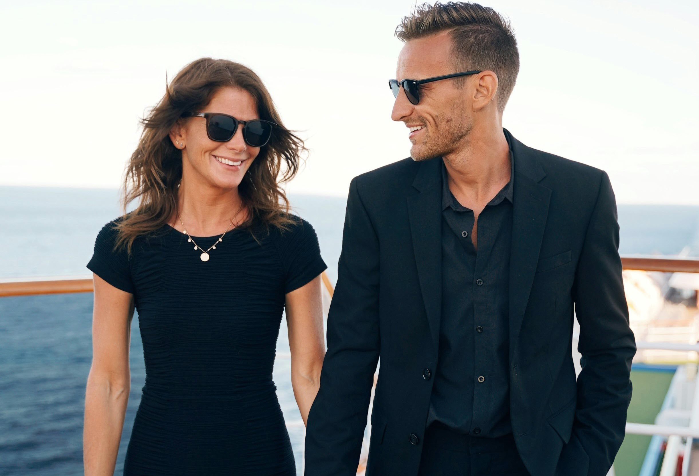 a man and woman wearing sunglasses and standing on a cruise deck