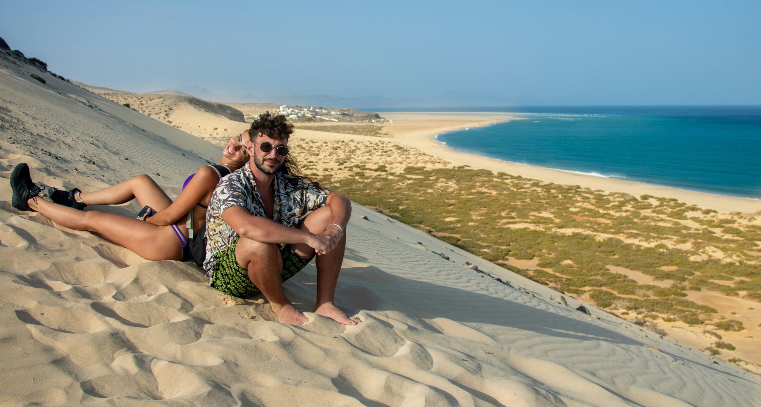 a man and woman sitting on the sand of a beach