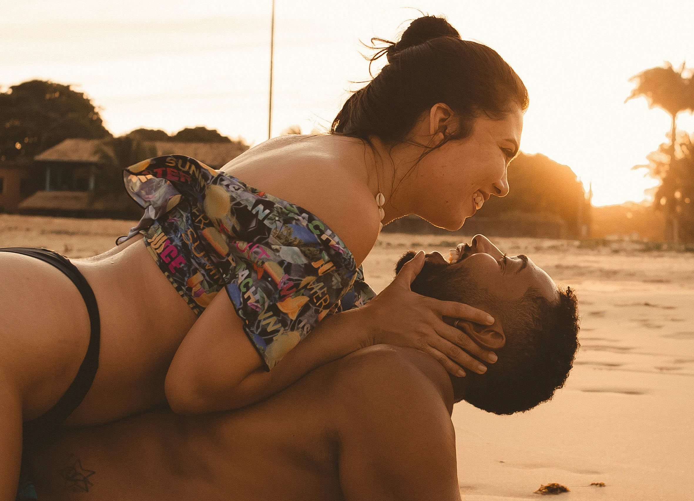 woman in black and white floral bikini sitting on beach sand during sunset