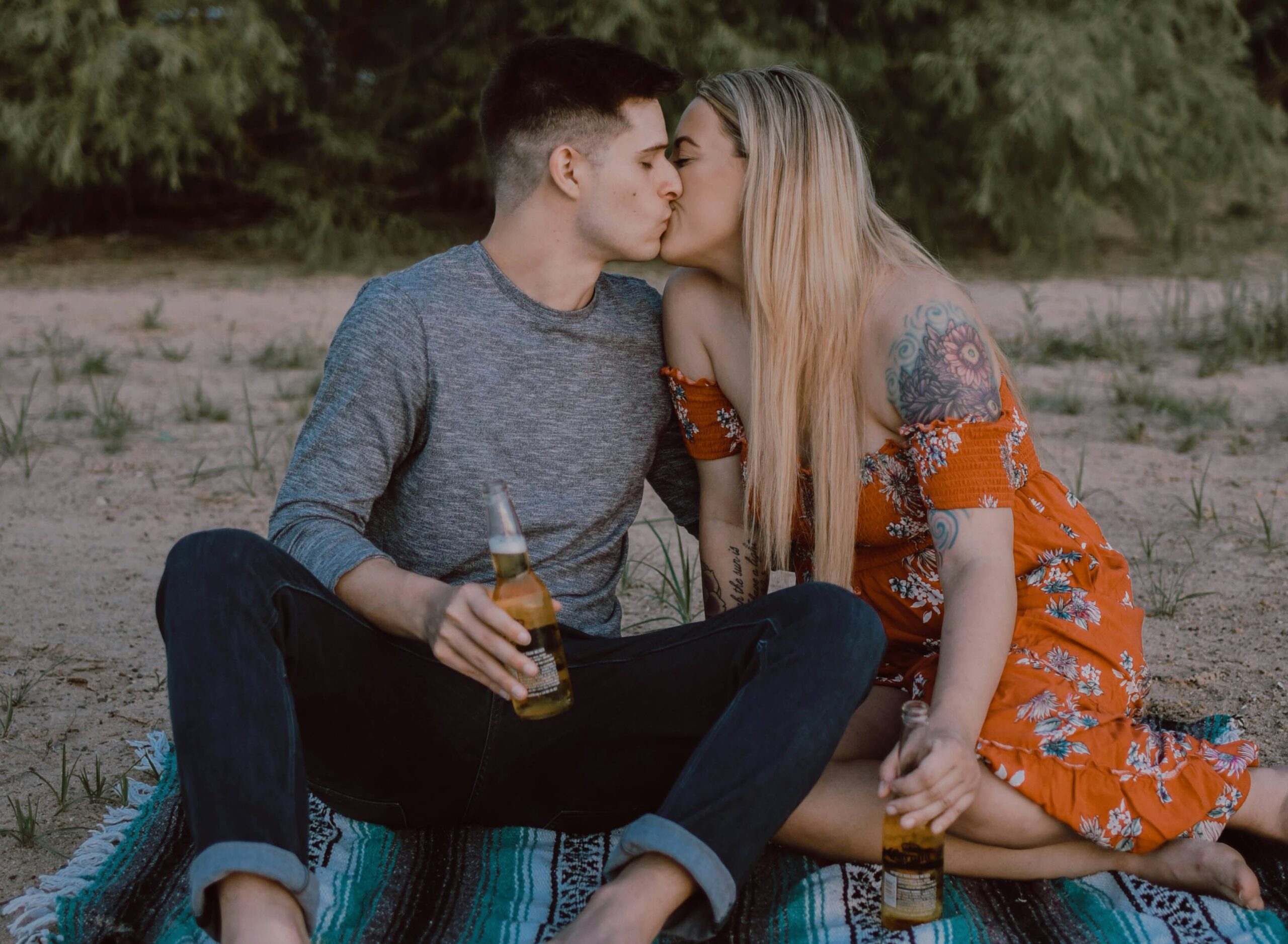 man and woman sitting while kissing on ground