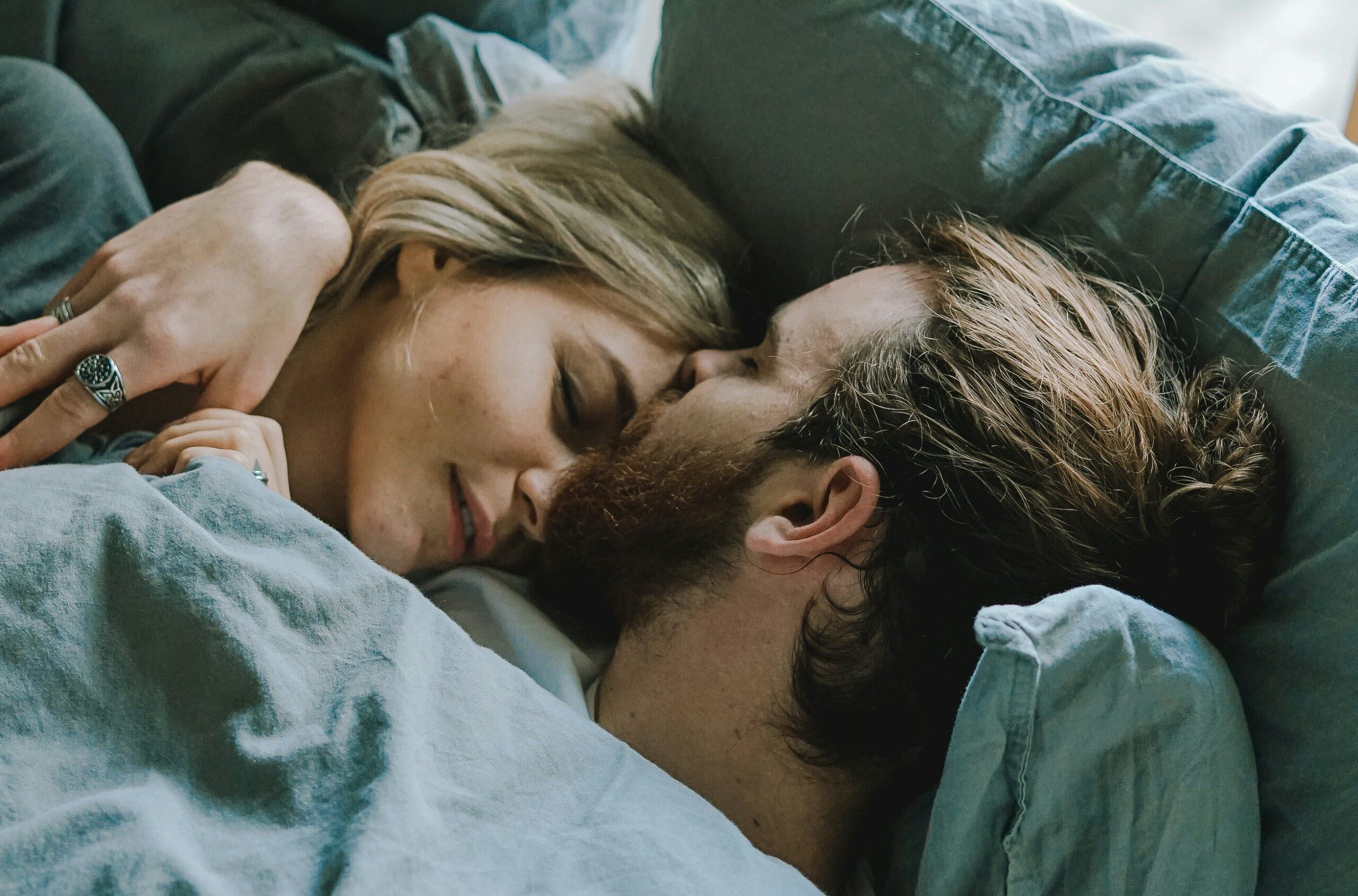 man kissing womans forehead while laying in bed