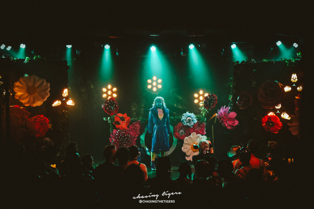 Image of a performer in the stage wearing mask with flower backdrop