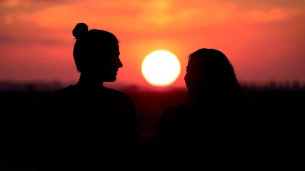 Couple silhouetted against a sunset, touching arms.