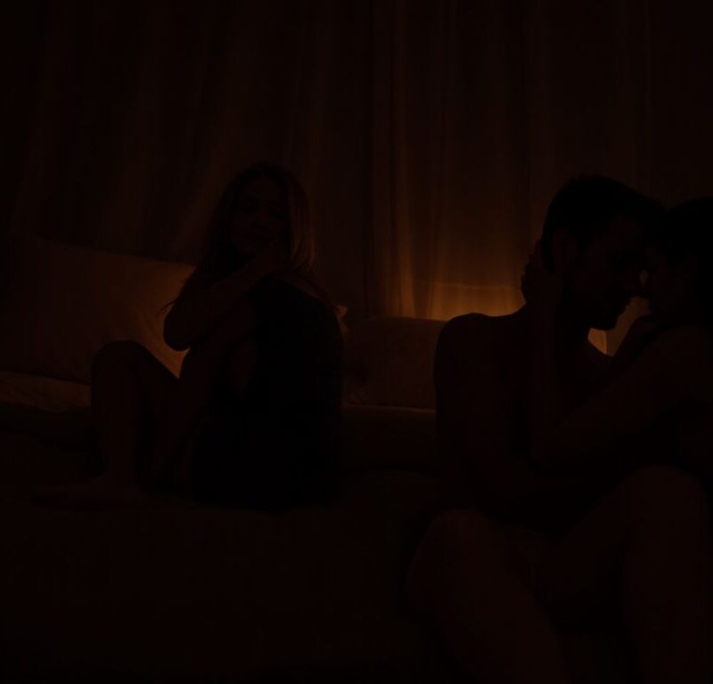 Two couples embracing intimately in a dimly lit bedroom.