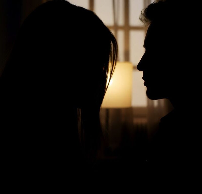Two silhouetted figures in a dimly lit, intimate setting.