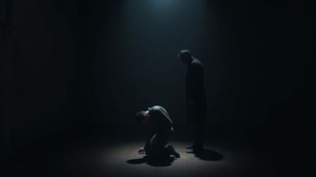 Man kneeling in submission, another figure standing over him.