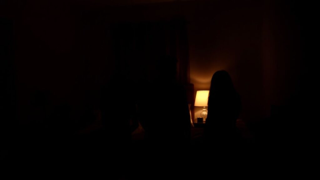 Three figures in a dimly lit bedroom, suggesting polyamory.