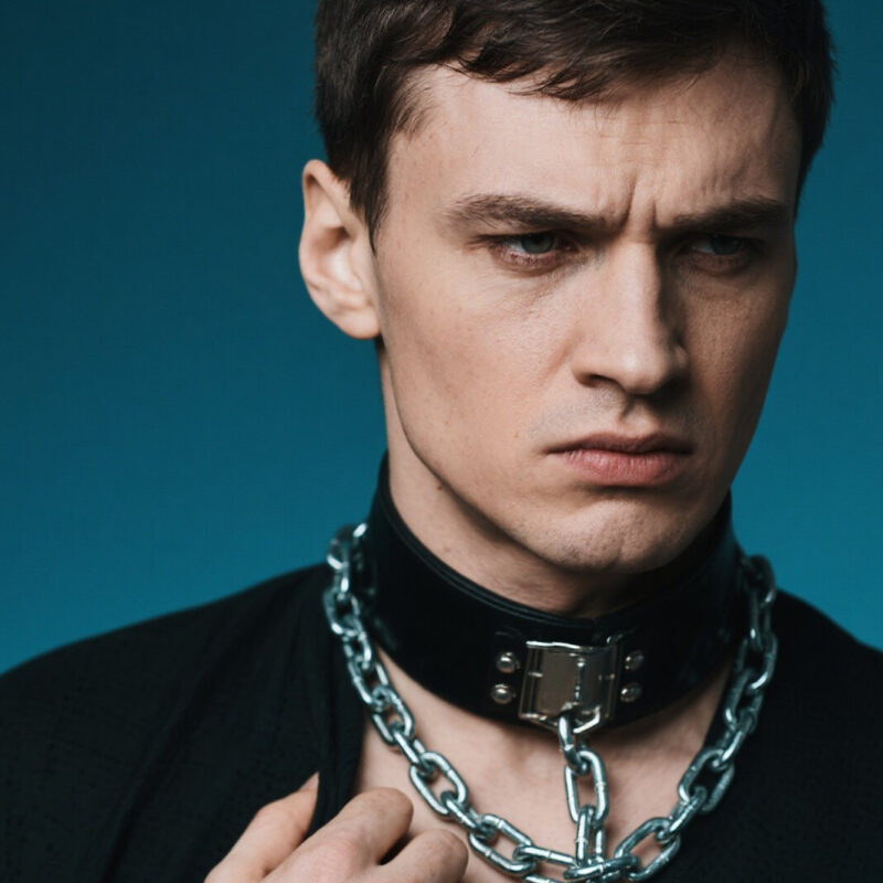 Man in collar and chains, conflicted expression.
