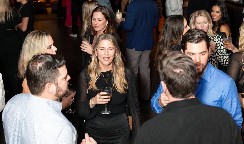 A stylish crowd of well-dressed couples mingles and laughs in the warmly lit lounge area of an upscale lifestyle club during a themed night out