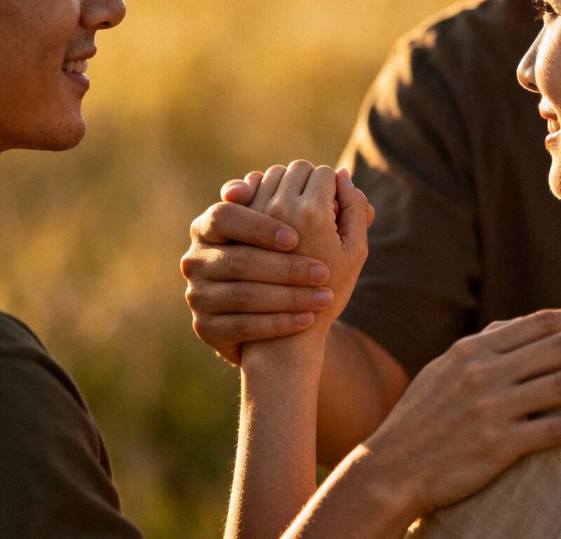 Couple holding hands, third person's hand on shoulder.