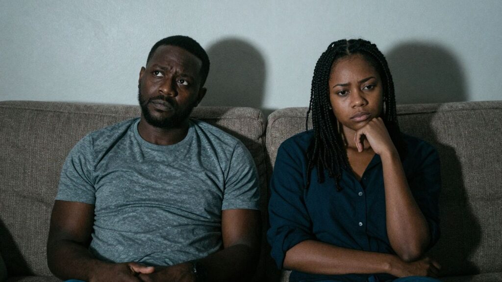 Couple looking away, third party looms behind them.