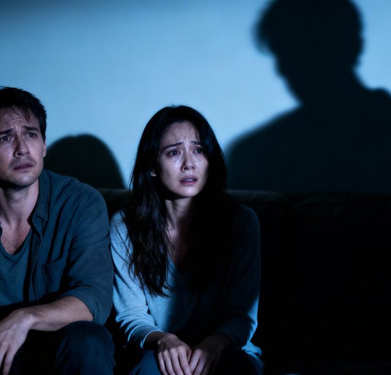 Couple on couch with shadowy figure behind them.