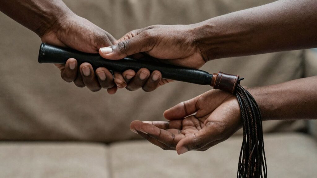 Hands holding a leather flogger, intimate atmosphere.