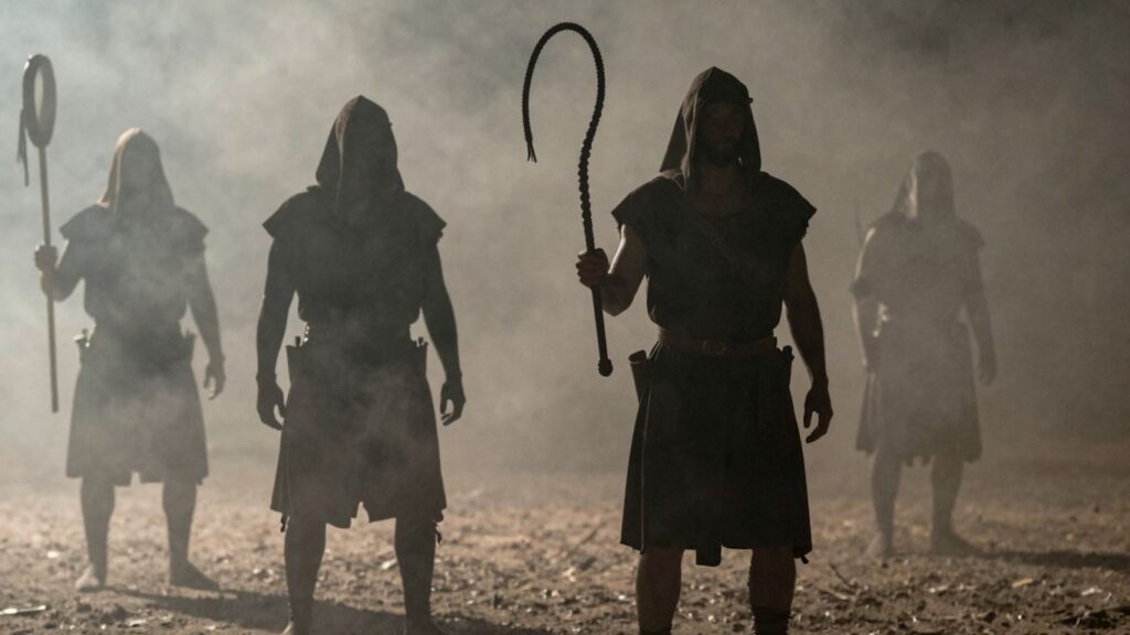 Historical figures and a whip in dim light.