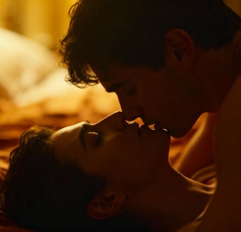 Couple embracing intimately in a warm, soft-lit bedroom.