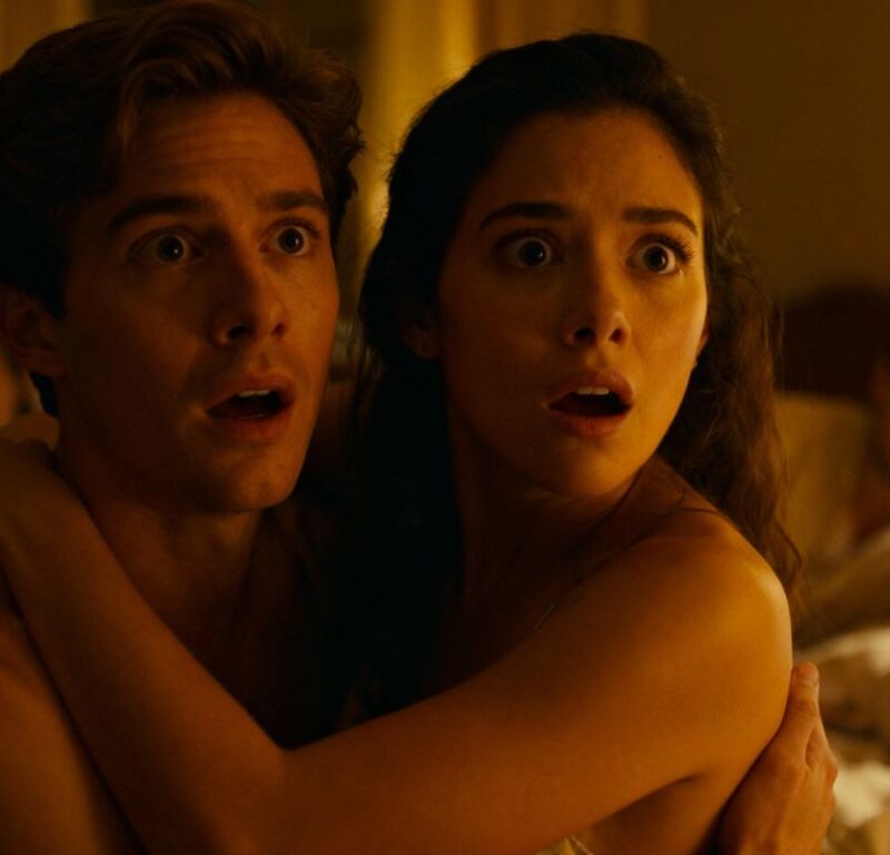 Couple in bedroom with others, intimate atmosphere.