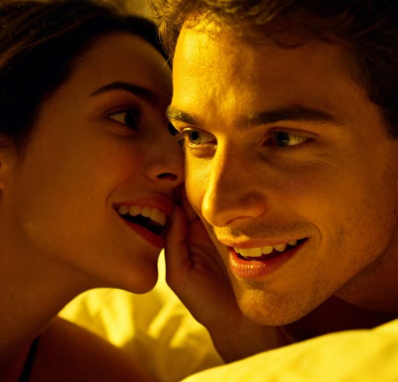 Couple whispering intimately in bed, testing compatibility.
