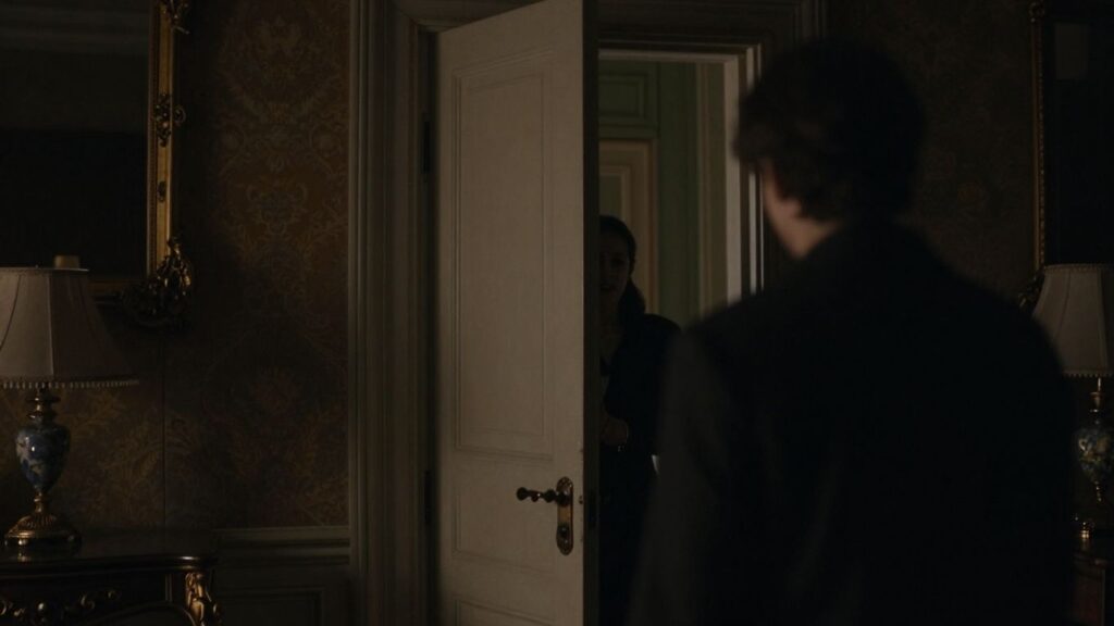 Two figures in a dimly lit room, one near a door.